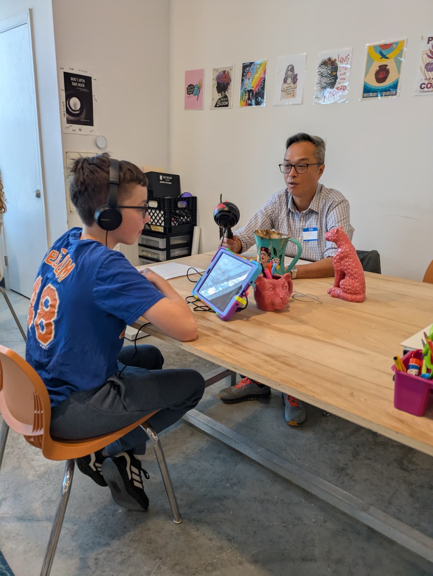 A young DJ in headphones interviewing an adult guest across a studio table